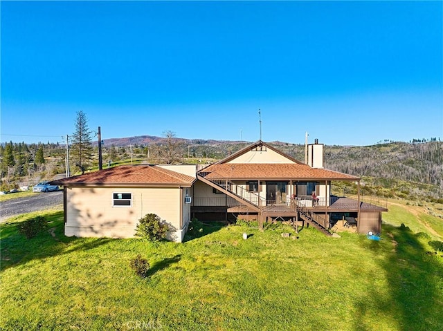 back of house with a deck with mountain view and a lawn