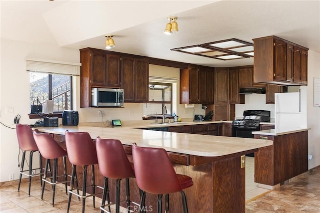 kitchen with lofted ceiling, sink, black gas range oven, a kitchen breakfast bar, and kitchen peninsula