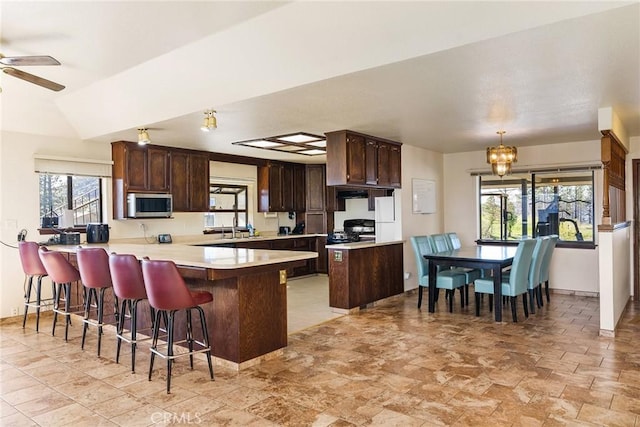 kitchen with range, a kitchen bar, decorative light fixtures, vaulted ceiling, and kitchen peninsula