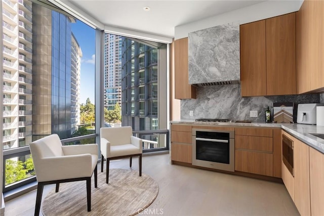 kitchen featuring stainless steel appliances, wall chimney range hood, a wall of windows, backsplash, and light wood-type flooring