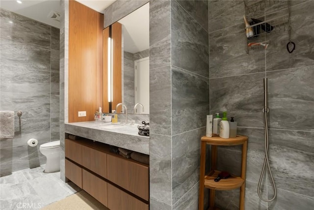 bathroom with vanity, a shower, toilet, and tile walls