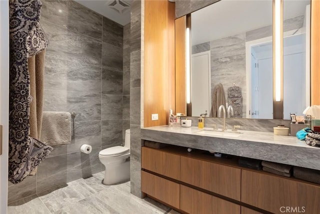 bathroom with vanity, toilet, and tile walls