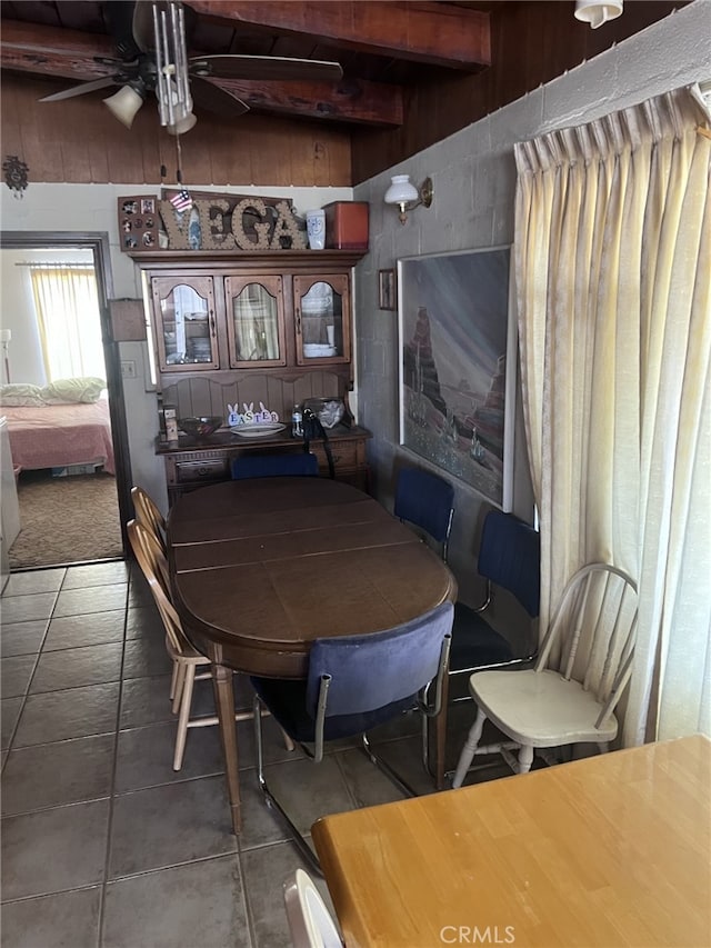 tiled dining area featuring ceiling fan, beam ceiling, and wooden walls