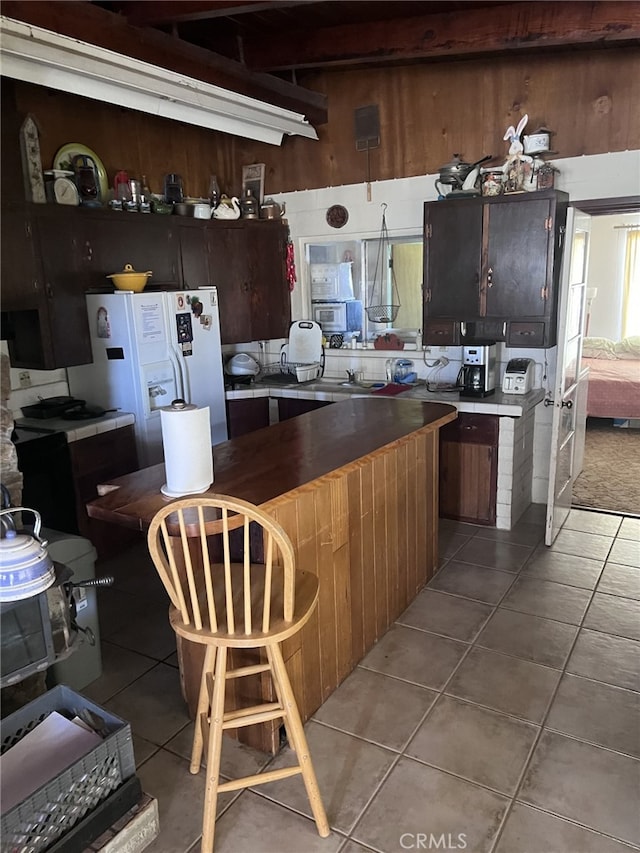 kitchen featuring light tile patterned floors, white refrigerator with ice dispenser, and wooden walls