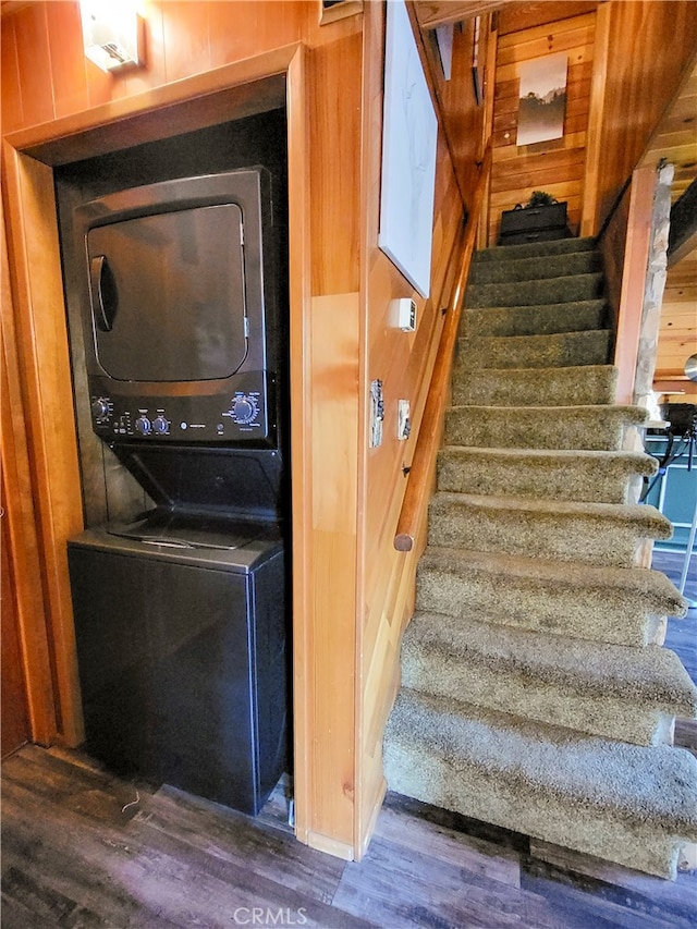 stairway featuring wooden walls, stacked washing maching and dryer, and hardwood / wood-style floors