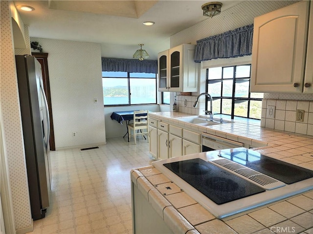 kitchen with dishwashing machine, tile countertops, stainless steel refrigerator, and sink