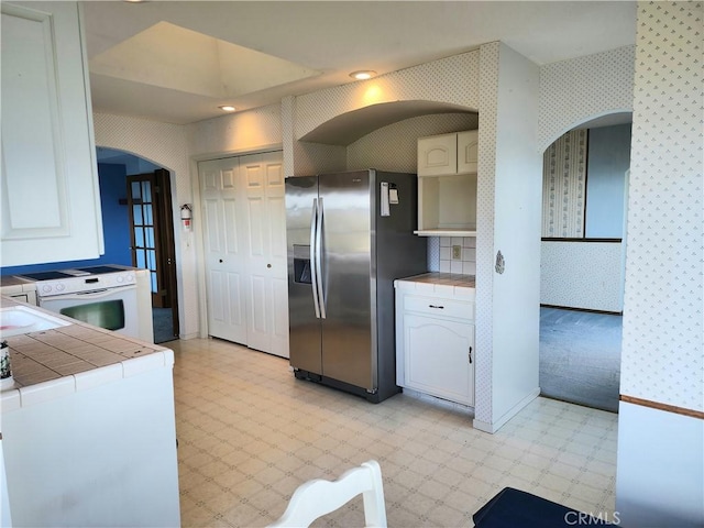 kitchen with electric stove, stainless steel fridge with ice dispenser, white cabinetry, tile counters, and washer / dryer