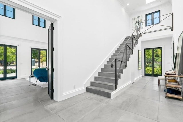 stairs with a high ceiling, crown molding, a skylight, and french doors