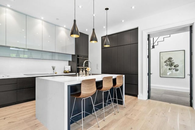 kitchen featuring a kitchen island with sink, a breakfast bar area, light wood-type flooring, and decorative light fixtures