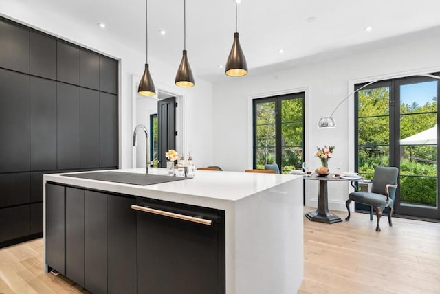 kitchen with pendant lighting, black dishwasher, a center island with sink, and light hardwood / wood-style floors