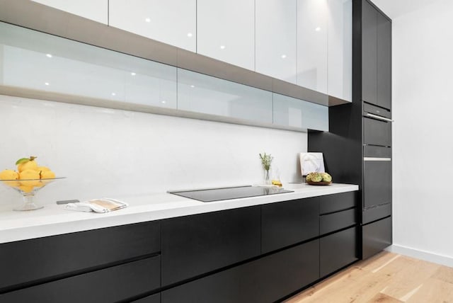 kitchen with black electric stovetop, light hardwood / wood-style flooring, oven, and white cabinets