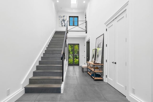 entryway featuring ornamental molding, a towering ceiling, and a skylight