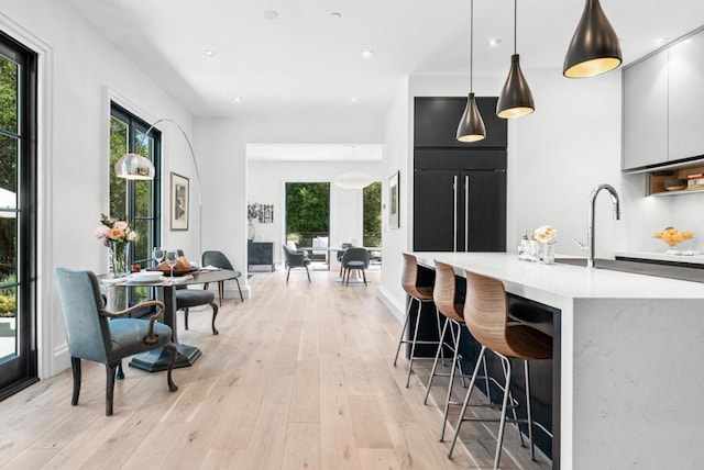 kitchen with a breakfast bar, pendant lighting, sink, paneled refrigerator, and light hardwood / wood-style flooring