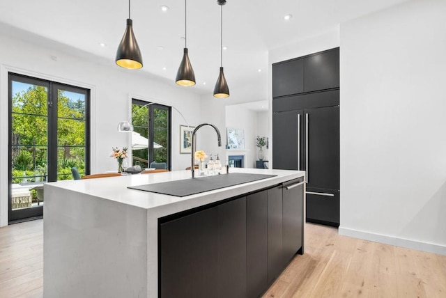 kitchen featuring hanging light fixtures, paneled fridge, a kitchen island with sink, and light wood-type flooring