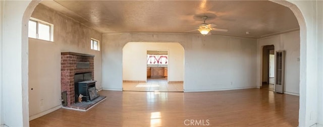 unfurnished living room featuring ceiling fan, a wood stove, and light hardwood / wood-style flooring