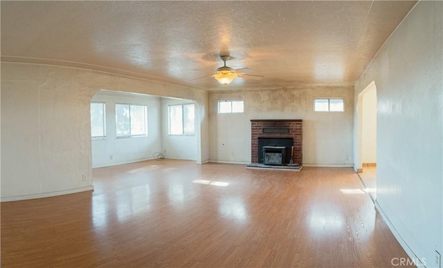 unfurnished living room featuring ceiling fan, light wood-type flooring, and a brick fireplace