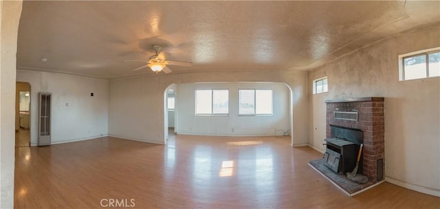 unfurnished living room featuring ceiling fan, a wood stove, and hardwood / wood-style floors