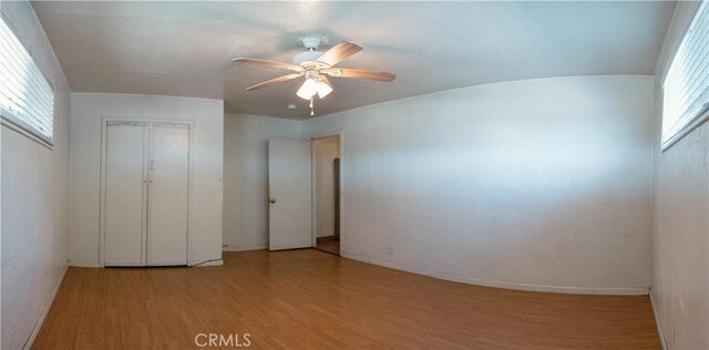 unfurnished bedroom featuring ceiling fan, multiple windows, a closet, and light wood-type flooring