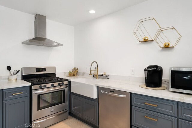 kitchen with light stone countertops, appliances with stainless steel finishes, wall chimney range hood, sink, and light hardwood / wood-style floors