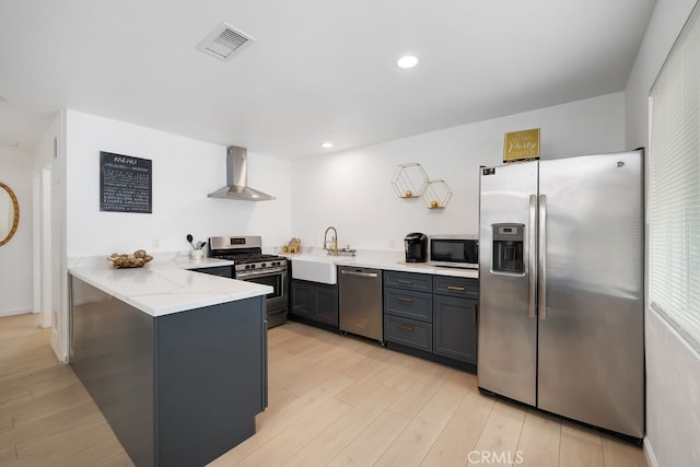 kitchen featuring light hardwood / wood-style flooring, appliances with stainless steel finishes, wall chimney range hood, sink, and light stone counters