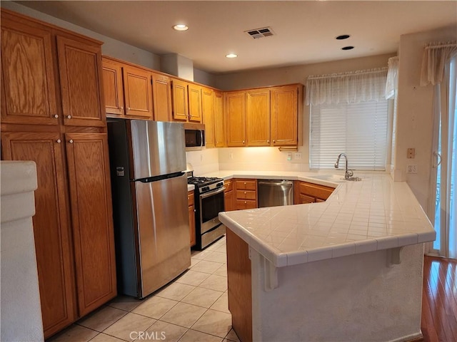 kitchen featuring tile countertops, sink, light tile patterned floors, kitchen peninsula, and stainless steel appliances