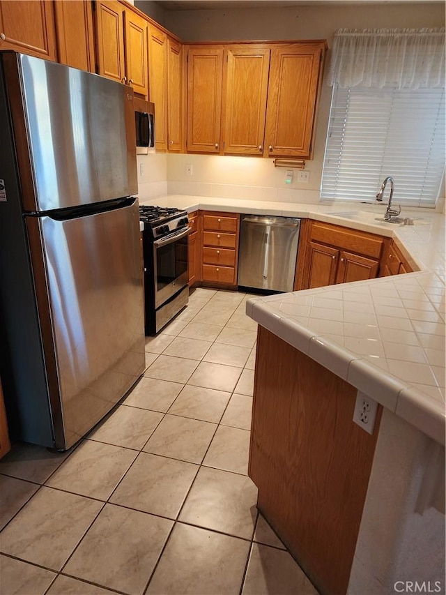 kitchen featuring tile counters, sink, kitchen peninsula, light tile patterned floors, and appliances with stainless steel finishes