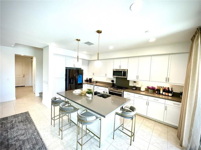 kitchen with appliances with stainless steel finishes, white cabinetry, a kitchen island with sink, and a kitchen breakfast bar