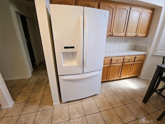 kitchen featuring white refrigerator with ice dispenser, tile countertops, and light tile patterned flooring