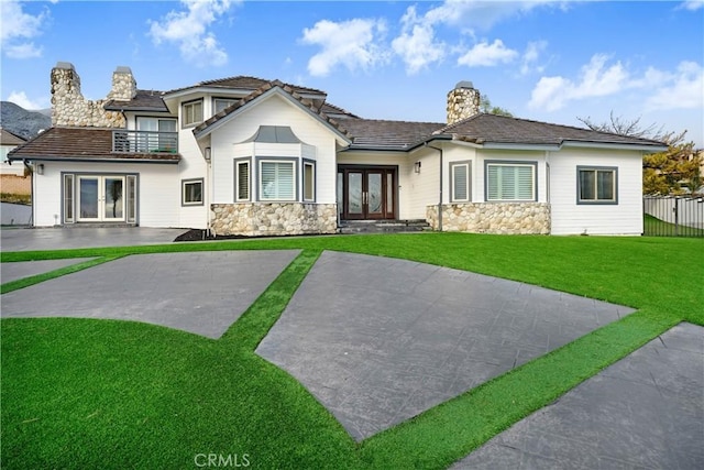 view of front of house featuring a front lawn, a balcony, and french doors