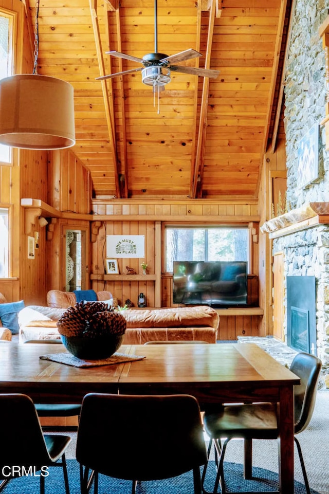 carpeted dining space with wood walls, wooden ceiling, beamed ceiling, and a fireplace