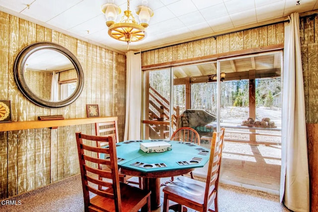 dining area featuring wooden walls, an inviting chandelier, and carpet flooring