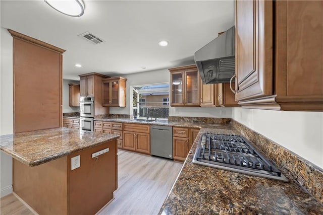 kitchen with kitchen peninsula, appliances with stainless steel finishes, light wood-type flooring, dark stone counters, and ventilation hood