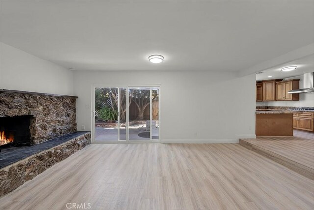 unfurnished living room featuring light wood-type flooring and a stone fireplace