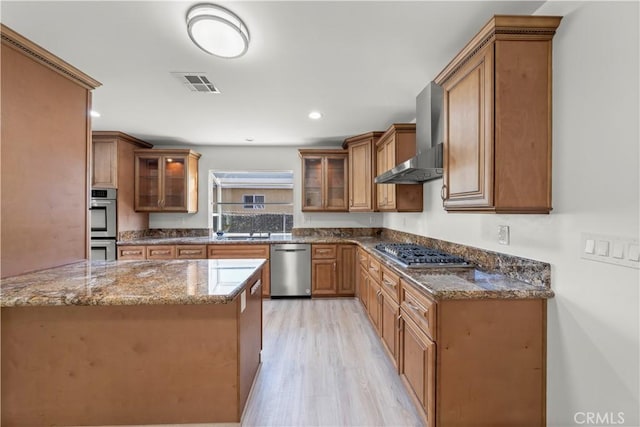 kitchen featuring appliances with stainless steel finishes, wall chimney range hood, sink, kitchen peninsula, and light hardwood / wood-style flooring