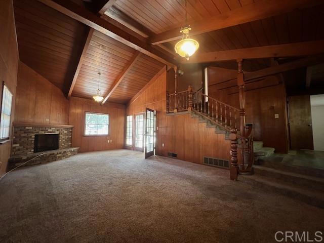 unfurnished living room featuring a stone fireplace, wood walls, carpet floors, vaulted ceiling with beams, and wood ceiling