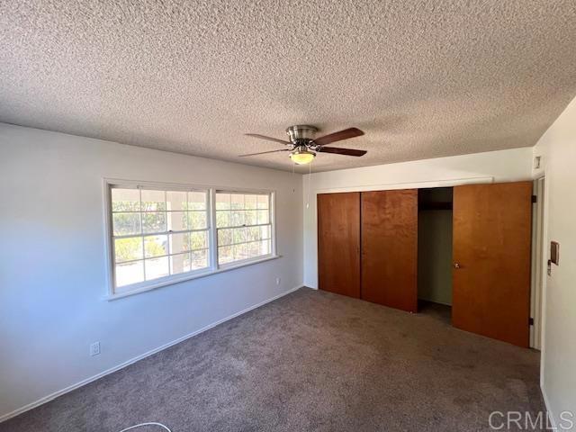 unfurnished bedroom featuring dark colored carpet, a textured ceiling, ceiling fan, and a closet