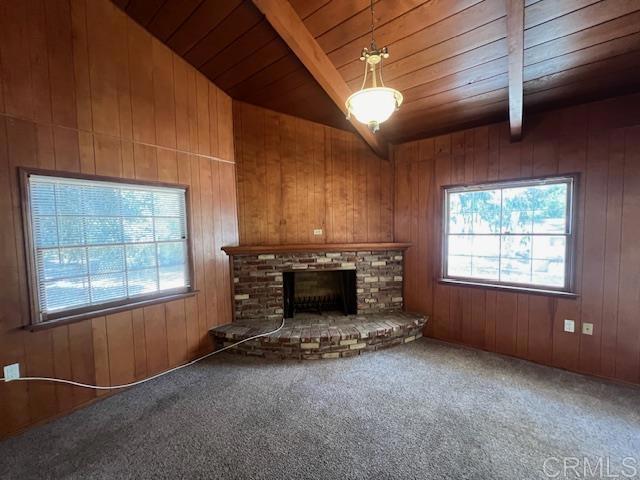 unfurnished living room featuring a brick fireplace, wood ceiling, a wealth of natural light, and carpet flooring