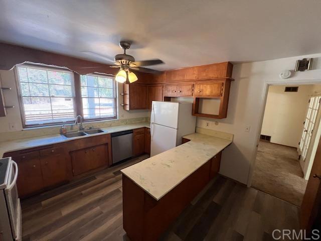 kitchen with sink, dark hardwood / wood-style flooring, ceiling fan, kitchen peninsula, and white appliances