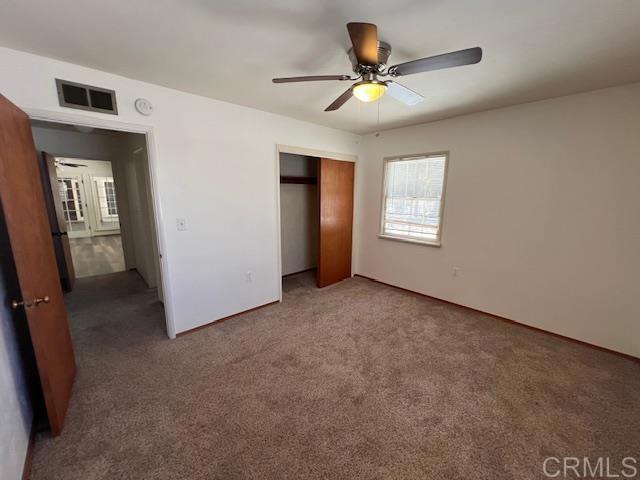 unfurnished bedroom with dark carpet, a closet, and ceiling fan