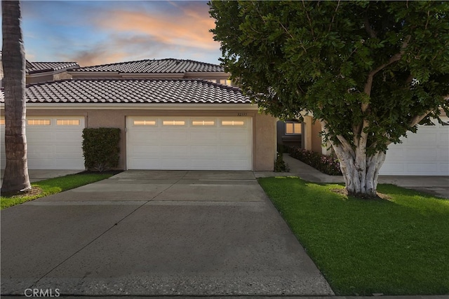 view of front of house with stucco siding, an attached garage, driveway, and a tiled roof