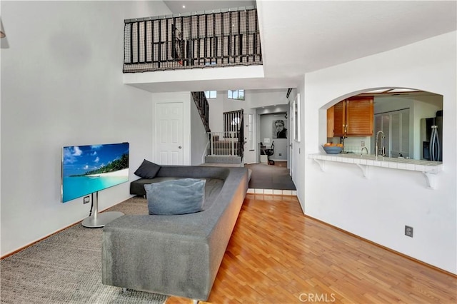 living area with stairway, arched walkways, light wood-type flooring, and a towering ceiling