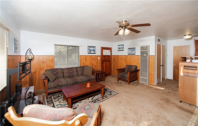 carpeted living room featuring ceiling fan, a textured ceiling, and wood walls