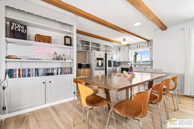 dining area with light hardwood / wood-style floors, beam ceiling, and sink