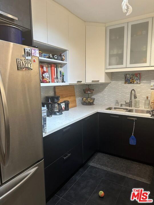 kitchen with white cabinets, dark tile flooring, stainless steel fridge, and tasteful backsplash