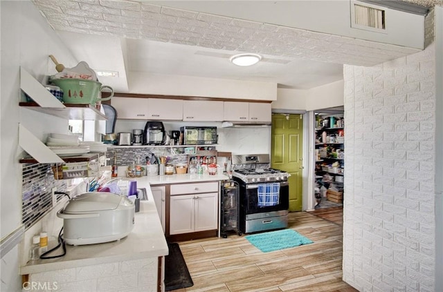 kitchen featuring stainless steel gas range oven, decorative backsplash, white cabinets, and light hardwood / wood-style floors