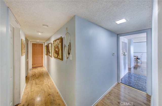 hallway with light hardwood / wood-style floors and a textured ceiling