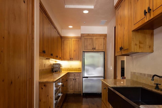 kitchen featuring light stone counters, sink, dark wood-type flooring, and stainless steel refrigerator