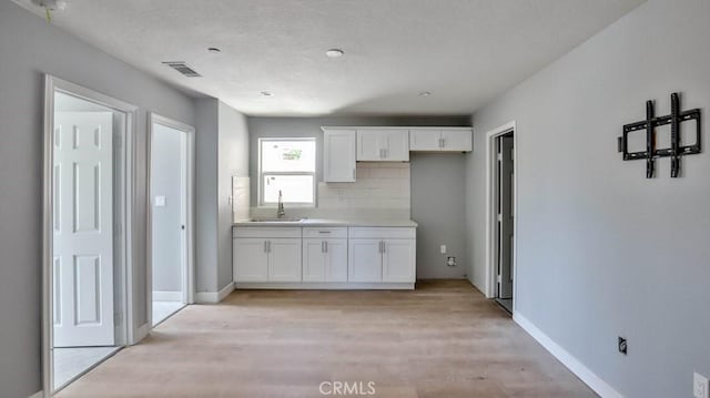 kitchen with light wood-type flooring, tasteful backsplash, white cabinetry, and sink