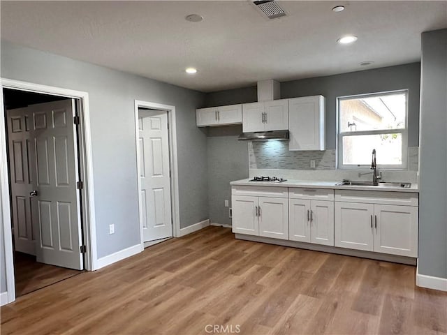 kitchen with sink, gas stovetop, light hardwood / wood-style floors, decorative backsplash, and white cabinets