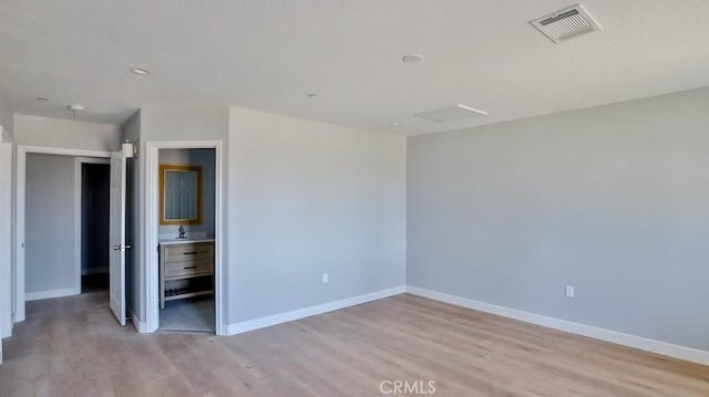 unfurnished bedroom featuring connected bathroom, sink, and light wood-type flooring